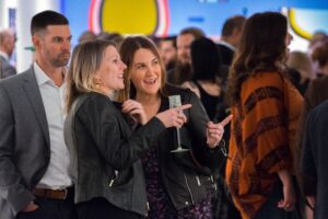 two woman smile as they discuss and admire an artwork at an art event