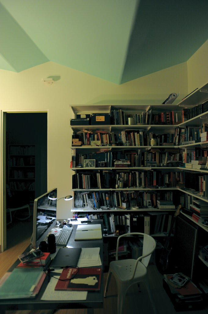 a cluttered industrial desk sits in front of two corner bookshelves