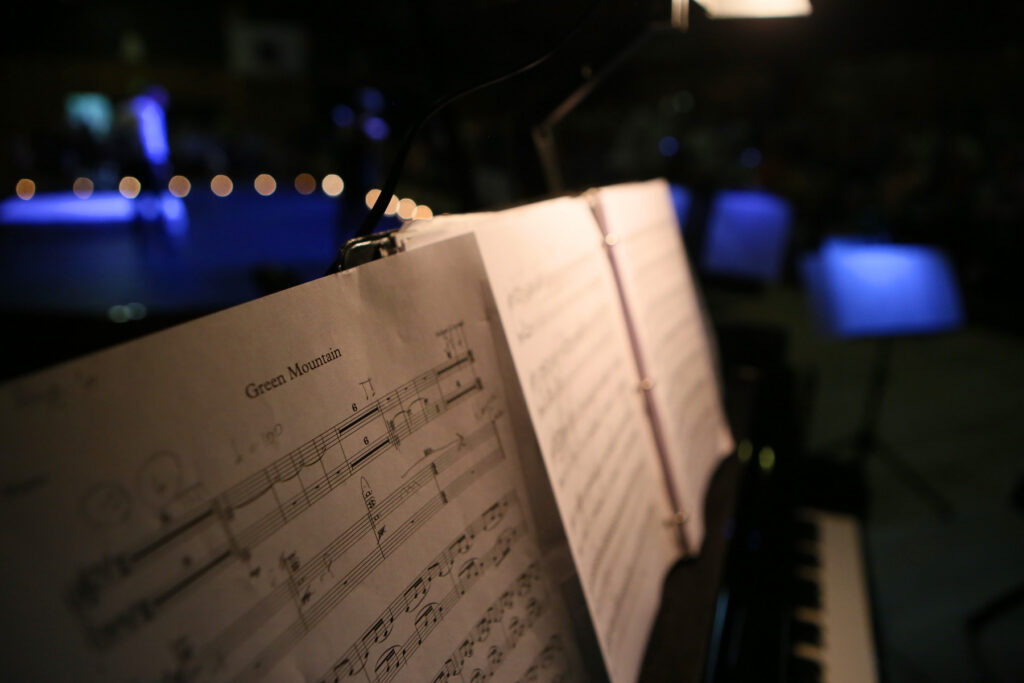 sheets of music on a music stand are dramatically lit in a dark space