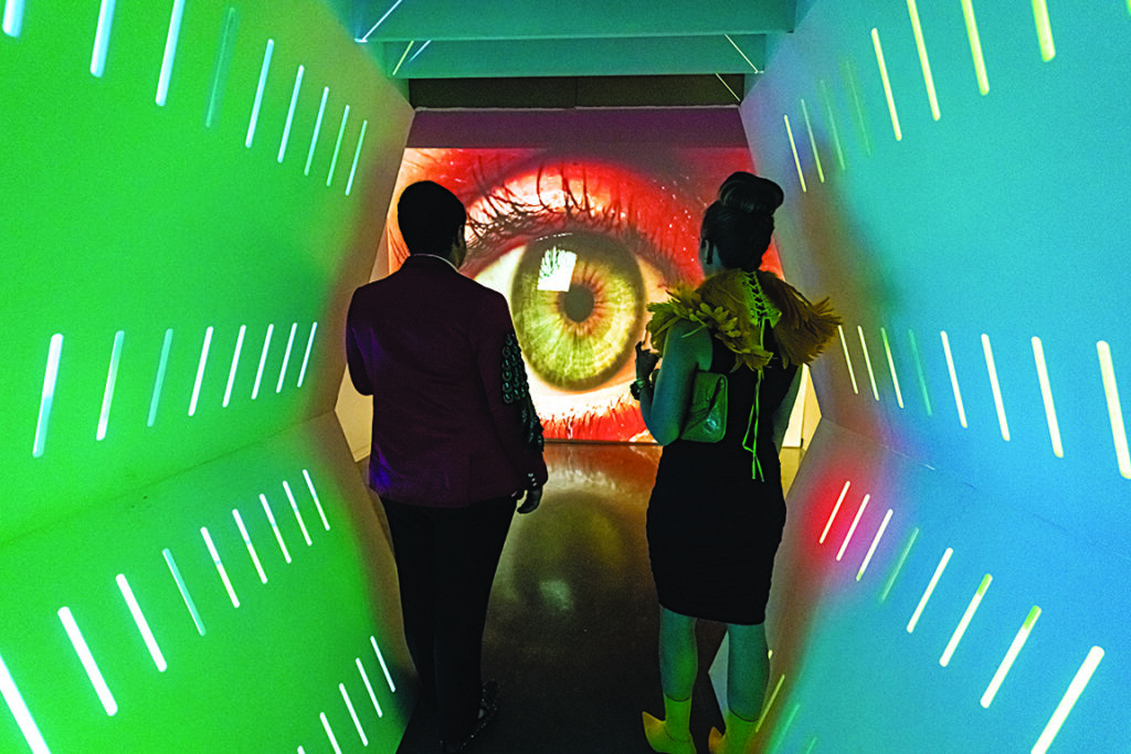 two people in a lighted tunnel look at a projection of an eye