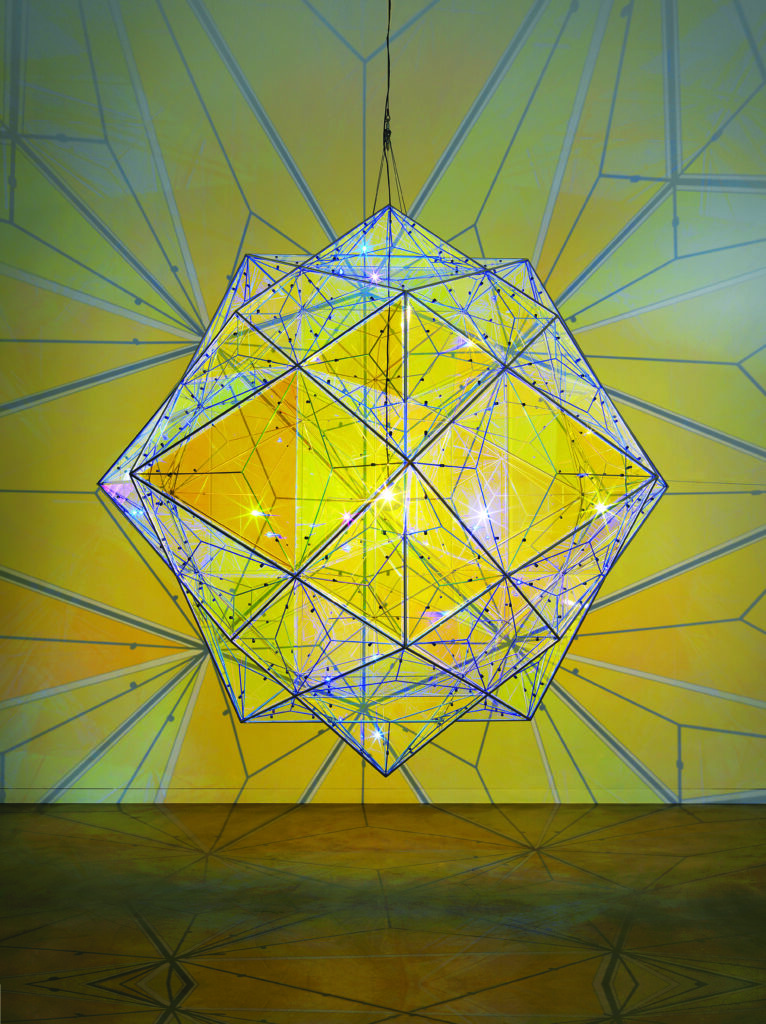 a giant star-like globe reflects golden light across a gallery space