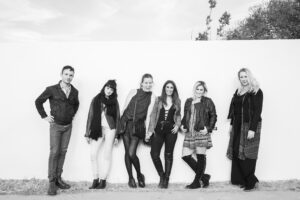 a group of trendy dressed young professionals lean against a white wall for a photo